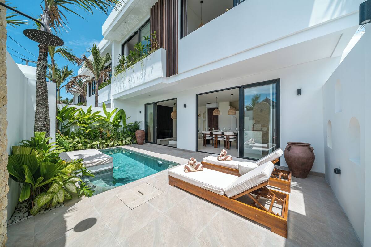 Un espace piscine extérieur moderne, doté de chaises longues, d’un coin repas et d’une végétation luxuriante.