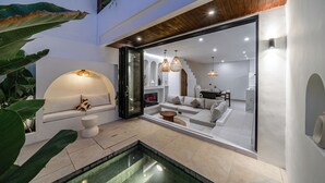 Un interior moderno con una zona de estar con paredes de vidrio, una piscina y un techo de madera.