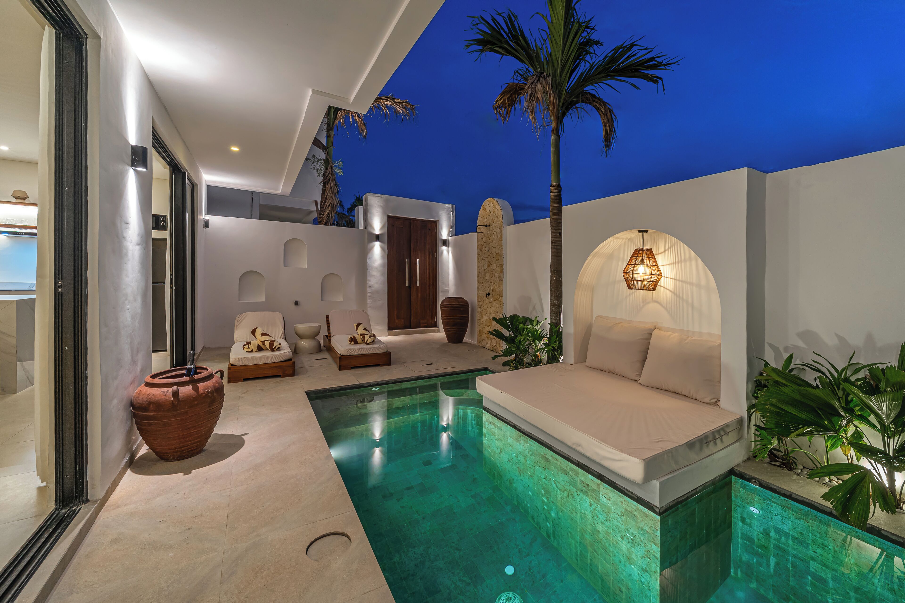 A modern outdoor pool area with a sofa, chairs, and a large planter.