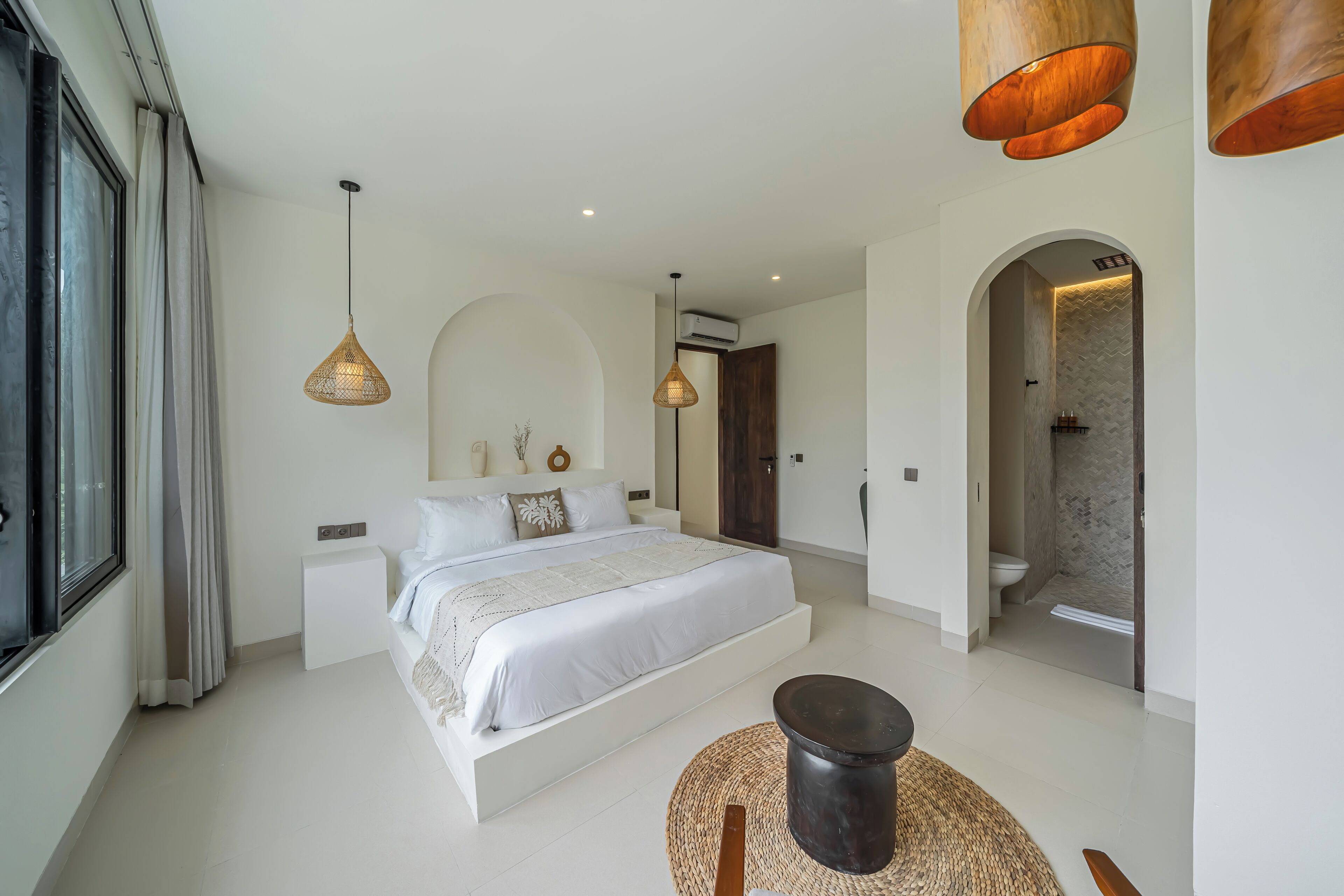 A modern bedroom with a large bed, bedside tables, a round seating area, and a shower.