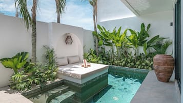 A private pool area with a sun lounger, surrounded by lush tropical plants and a large terracotta pot.