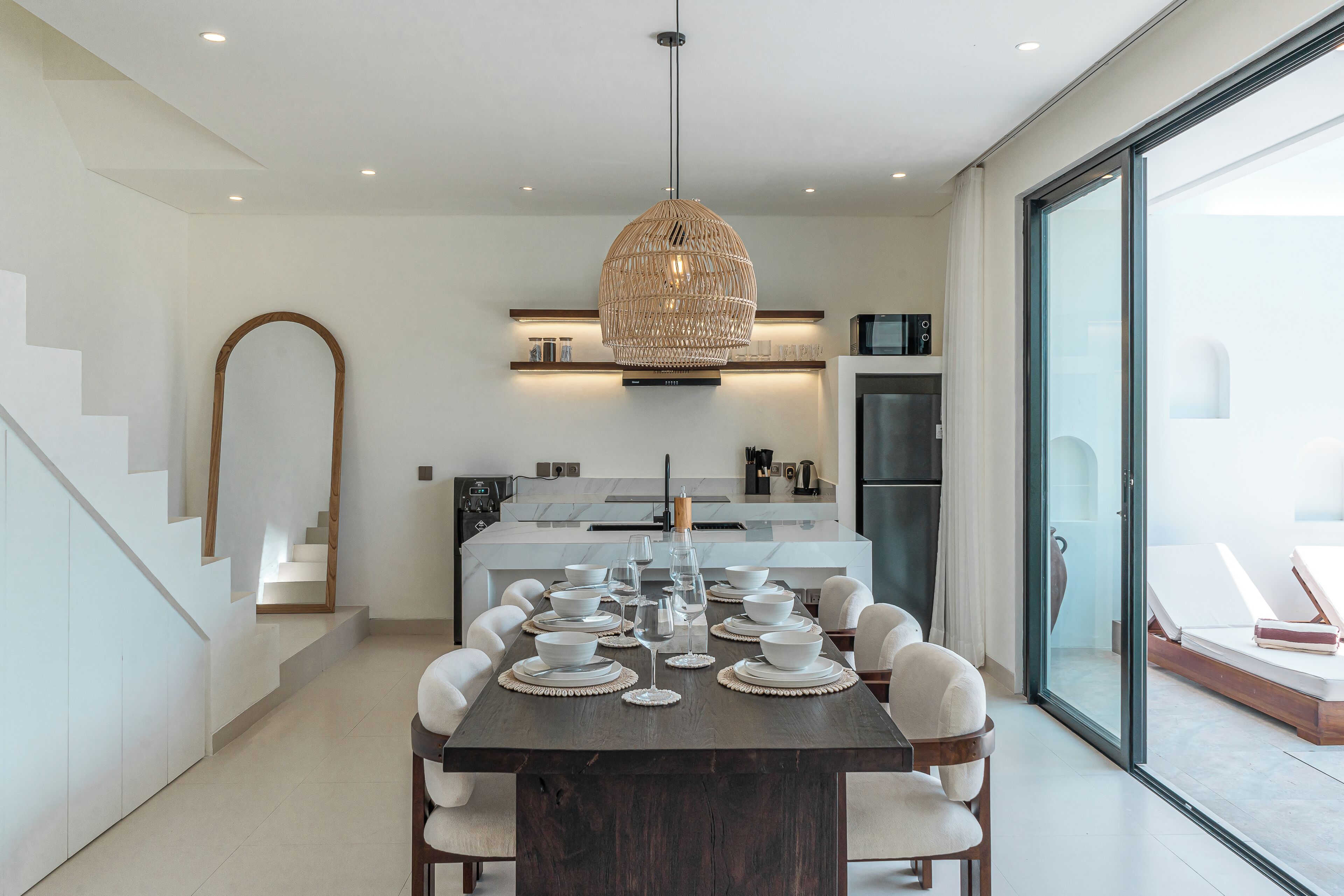A modern kitchen with a central island, white dining area, and a glass-enclosed balcony.