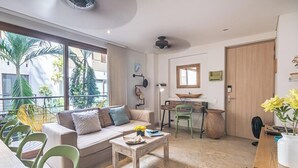 A modern living room with a sofa, coffee table, and chairs, a dining area with a table and chairs, and a large window with a view of palm trees. - Designer apartment with pool and private balcony (Santa Marta)