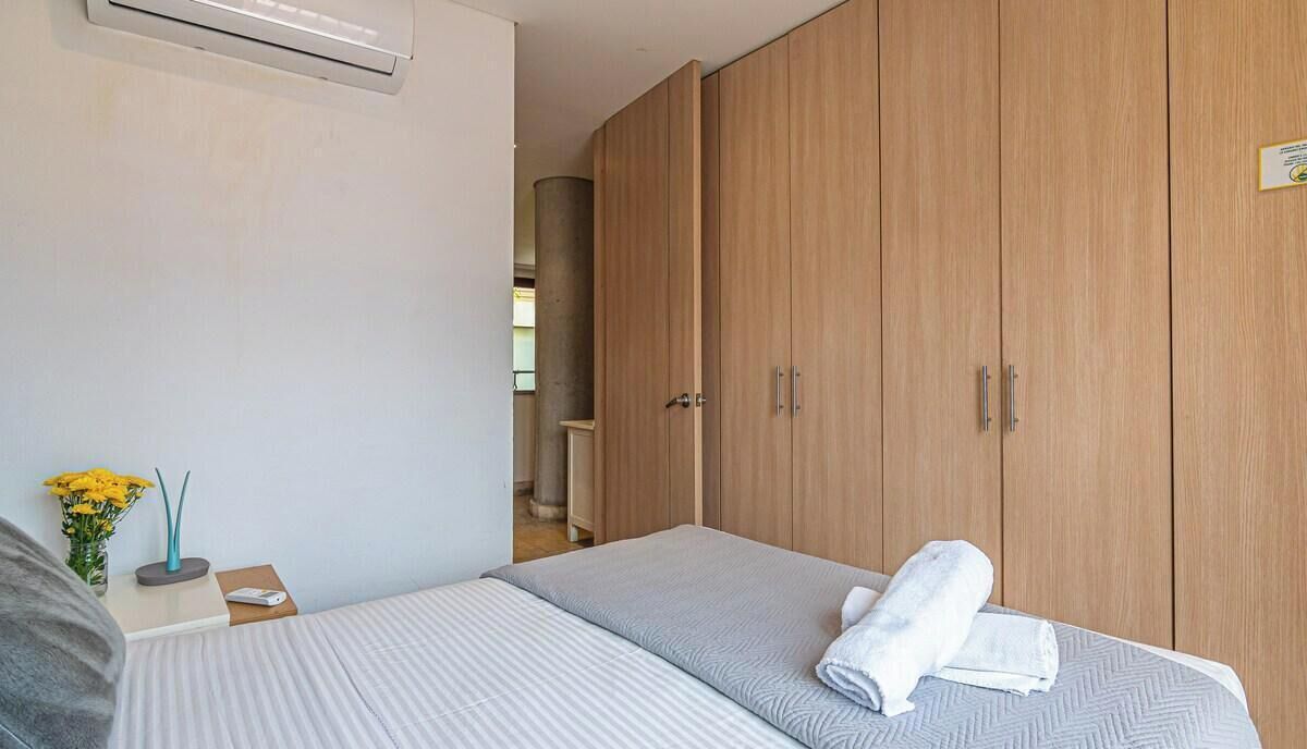 Habitación de hotel con una cama, un armario de madera, una mesita de noche con un jarrón de flores amarillas y un aire acondicionado de pared.