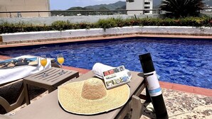 A poolside area with a lounge chair, a straw hat, a magazine, and a bottle. - Designer apartment with pool and private balcony (Santa Marta)