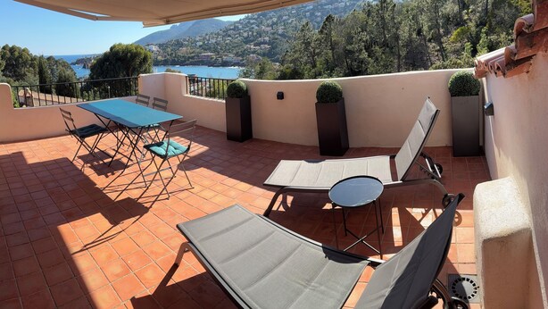 A terrace with a table and chairs, a sun lounger, and a view of a lake and mountains. - Paradise on the sea (Théoule-sur-Mer)
