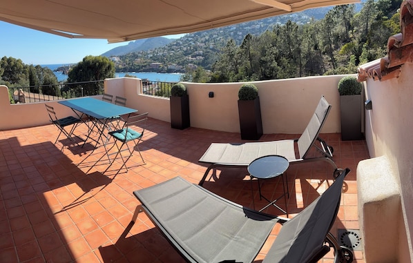 Eine Terrasse mit Tisch und Stühlen, einer Liege und Blick auf einen See und Berge.