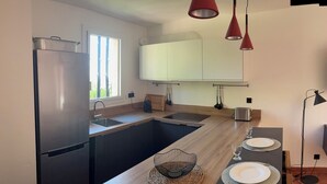 A modern kitchen with a stainless steel refrigerator, wooden countertops, a built-in sink, and a dining area with two plates and glasses. - Paradise on the sea (Théoule-sur-Mer)