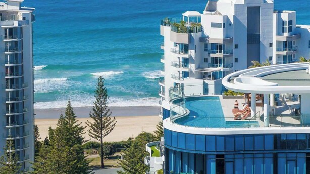 Un hotel modern amb piscina, vistes a la platja i diversos balcons.
