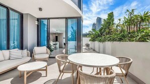Terrassa exterior moderna amb taula rodona i cadires de vimet, un sofà i una porta de vidre que dona a un espai interior.