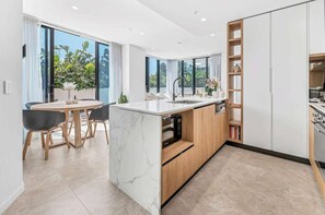A modern kitchen with a marble island, wooden cabinets, and a dining area with a table and chairs. - The Gallery Broadbeach (Broadbeach)