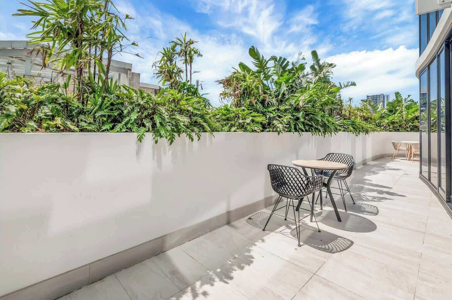 Eine Dachterrasse mit einer niedrigen Mauer, zwei Tischen mit Stühlen und üppiger Bepflanzung.