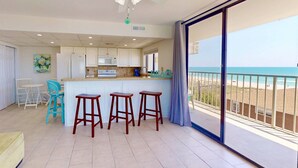 A kitchen with white cabinets, a white refrigerator, and a bar area with stools. - Top Floor Ocean View Corner Condo w/ Balcony, Pool & Elevator – Near Beach & CB Lake (Carolina Beach)