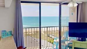 A balcony with a view of the beach and ocean, a ceiling fan, and a TV on a stand. - Top Floor Ocean View Corner Condo w/ Balcony, Pool & Elevator – Near Beach & CB Lake (Carolina Beach)