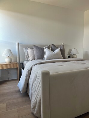 Un dormitorio con cama, almohadas, mesita de noche y lámpara.