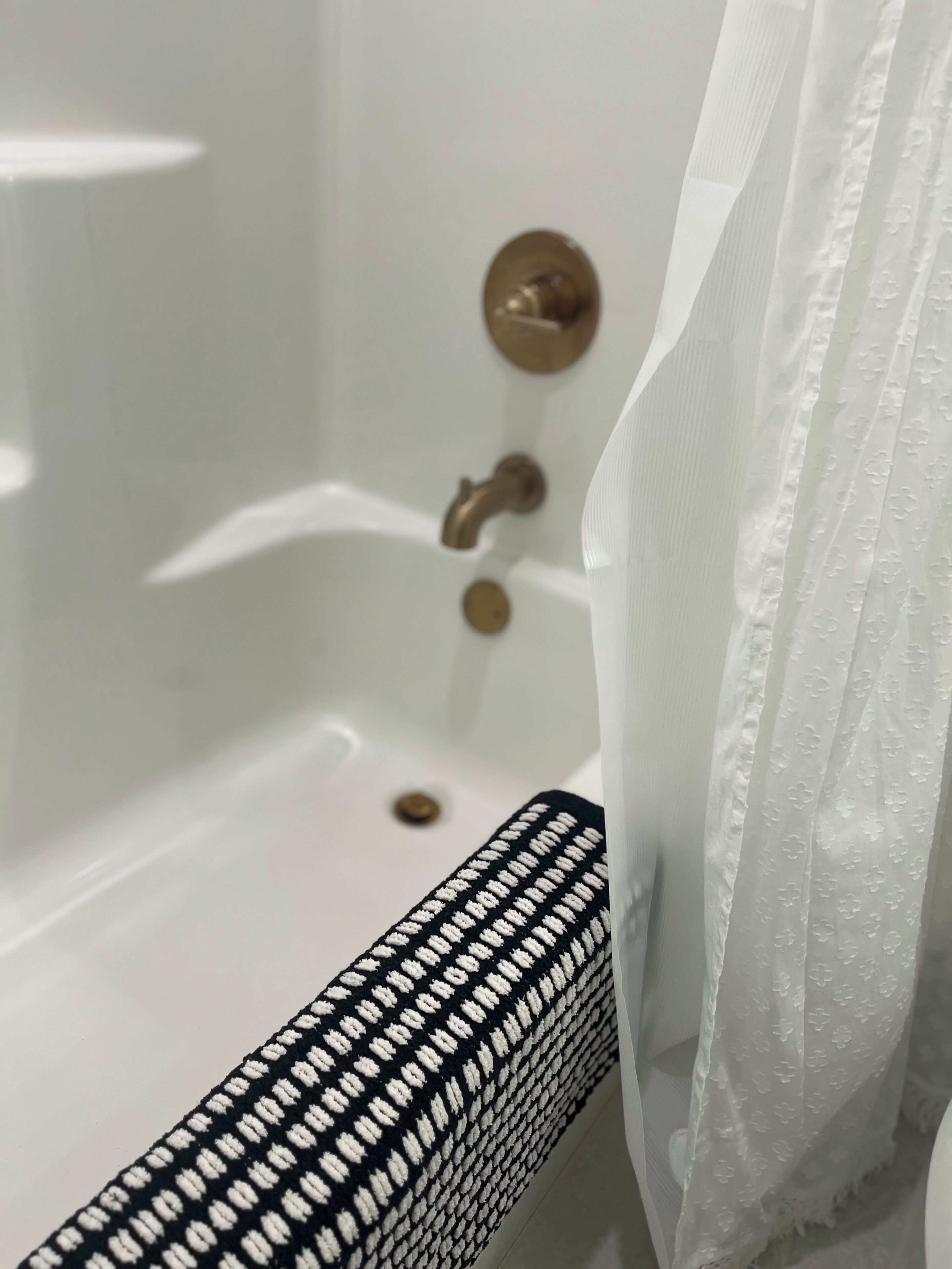 A bathtub with a brass faucet, a black and white patterned towel, and a white shower curtain.