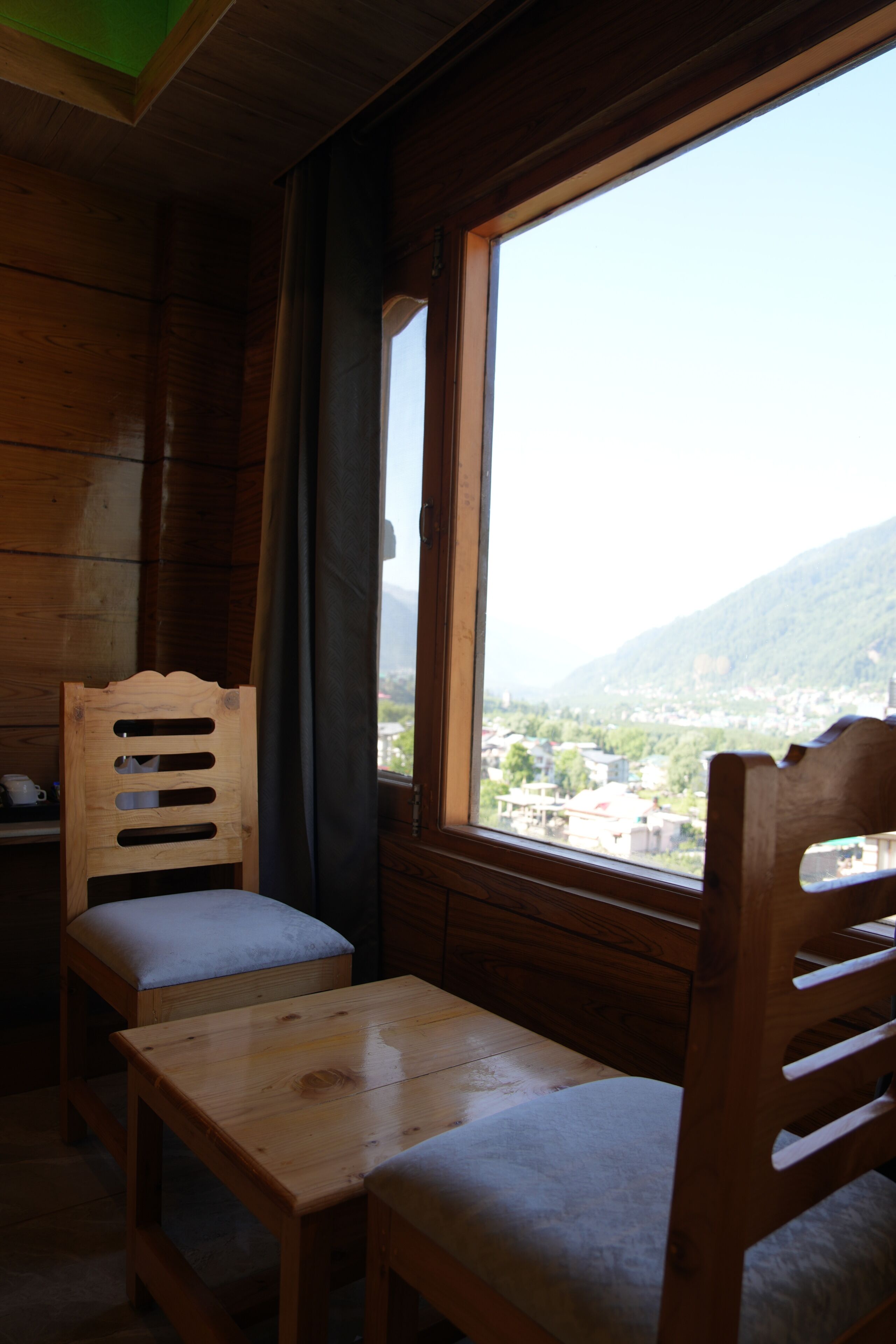 A wooden cabin interior with a window view of a town and mountains.