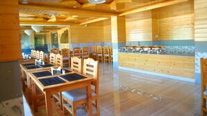 A wooden interior with a dining area featuring tables and chairs, a kitchen counter, and a ceiling with wooden beams and recessed lighting. - The Park Green Resorts (Manali)