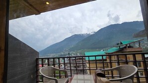 A balcony with two chairs, a view of a mountain range, and buildings in the background. - The Park Green Resorts (Manali)