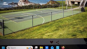 Een tennisbaan met uitzicht op de oceaan en een gebouw met een balkon.