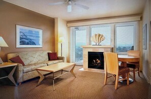 Een woonkamer met een bank, een salontafel, een open haard en een eethoek met stoelen.