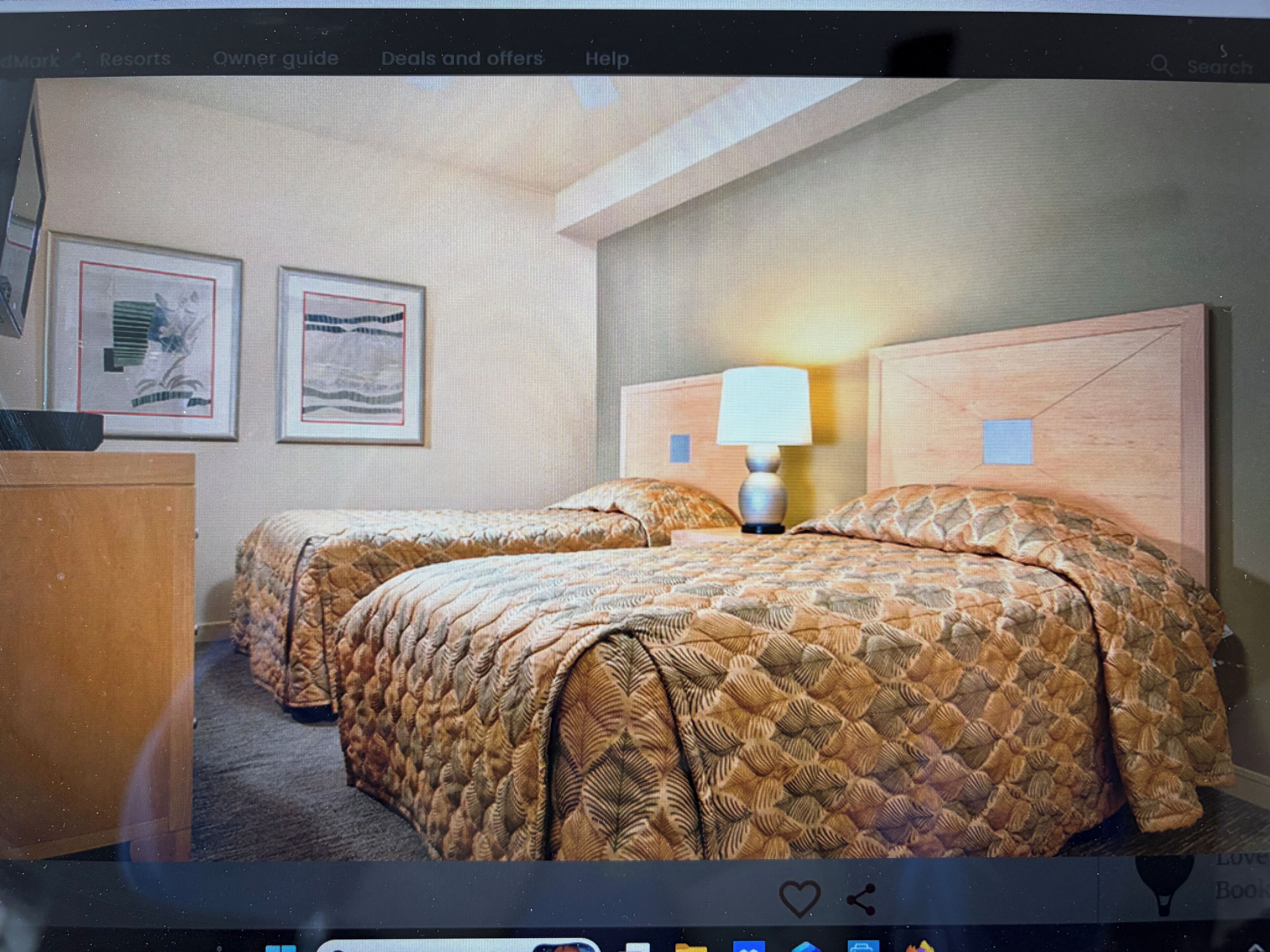 Ein Hotelzimmer mit zwei Betten, einem Schreibtisch, gerahmten Bildern an der Wand und einer Lampe.