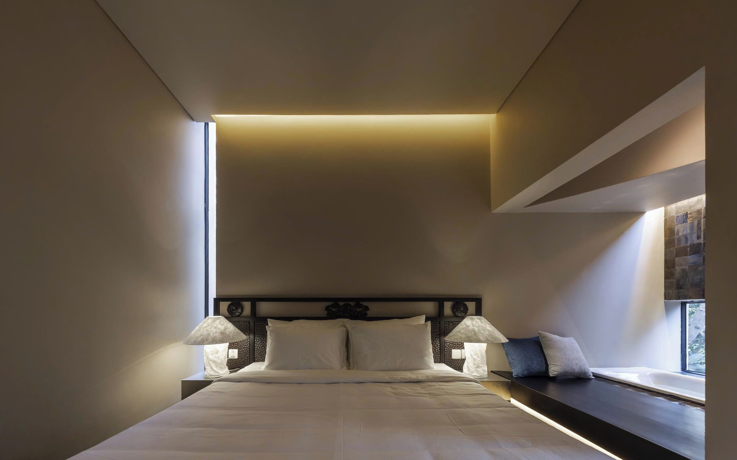 Una habitación de hotel moderna con una cama grande, dos lámparas de noche, un ventanal con vistas y un diseño de techo original.