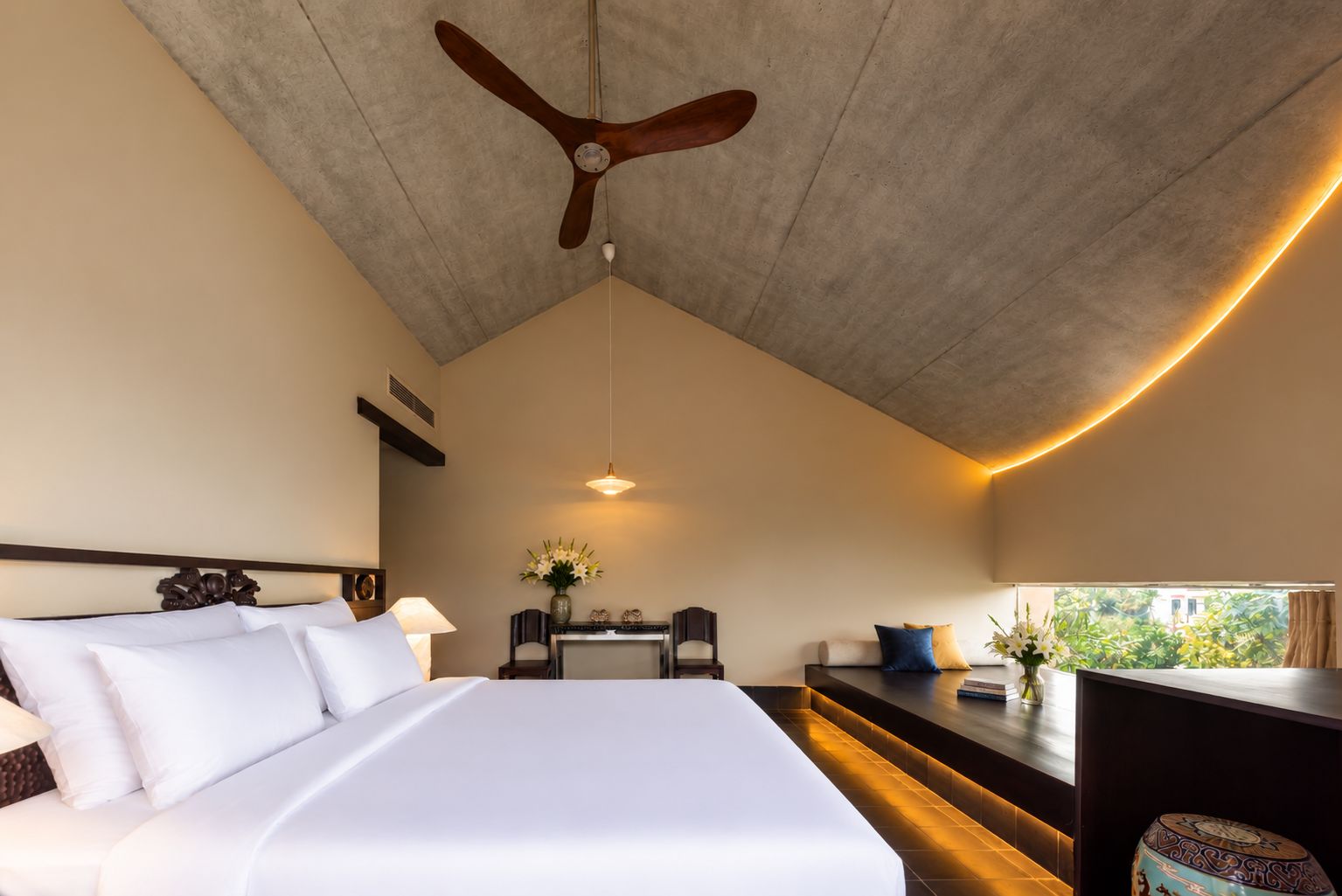 Une chambre d’hôtel équipée d’un lit, d’un bureau, d’une chaise, d’un ventilateur de plafond et d’une fenêtre donnant sur un paysage agréable.