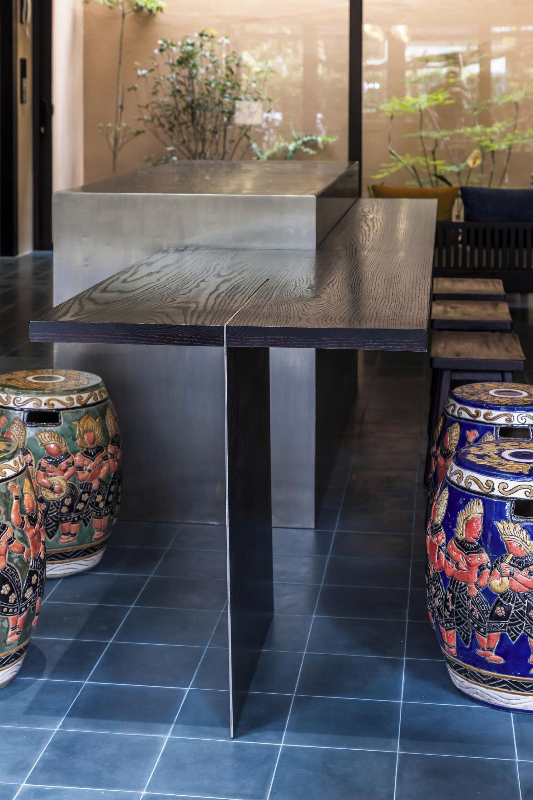 Un espace repas moderne avec une table en bois foncé, deux tabourets décoratifs et une vue sur la verdure grâce à une porte vitrée.
