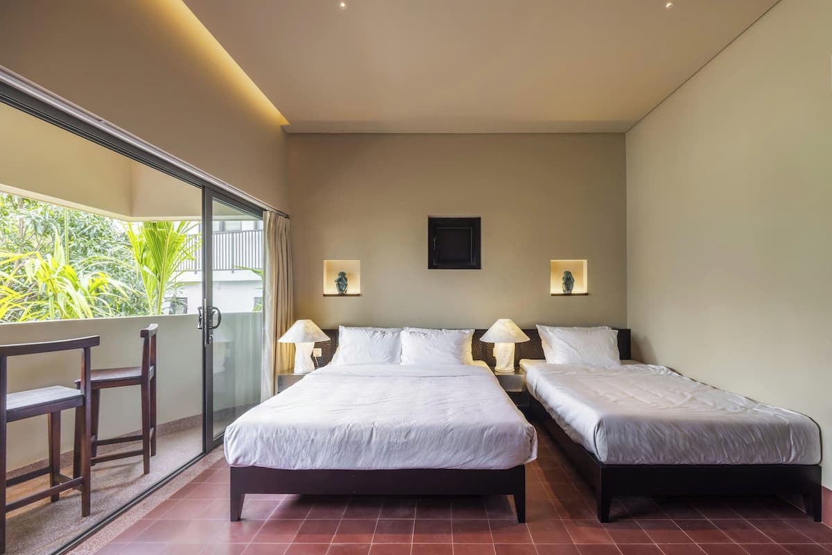 Habitación de hotel con dos camas, un balcón con una silla y vistas a zonas verdes.