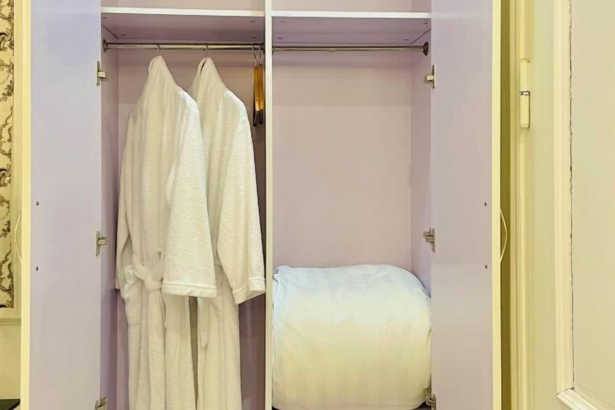 Un dressing où l’on peut entrer et qui contient des vêtements suspendus, ainsi qu’un lit.