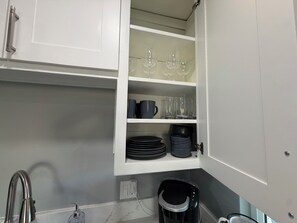 A kitchen with white cabinets, a coffee machine, and a trash bin.