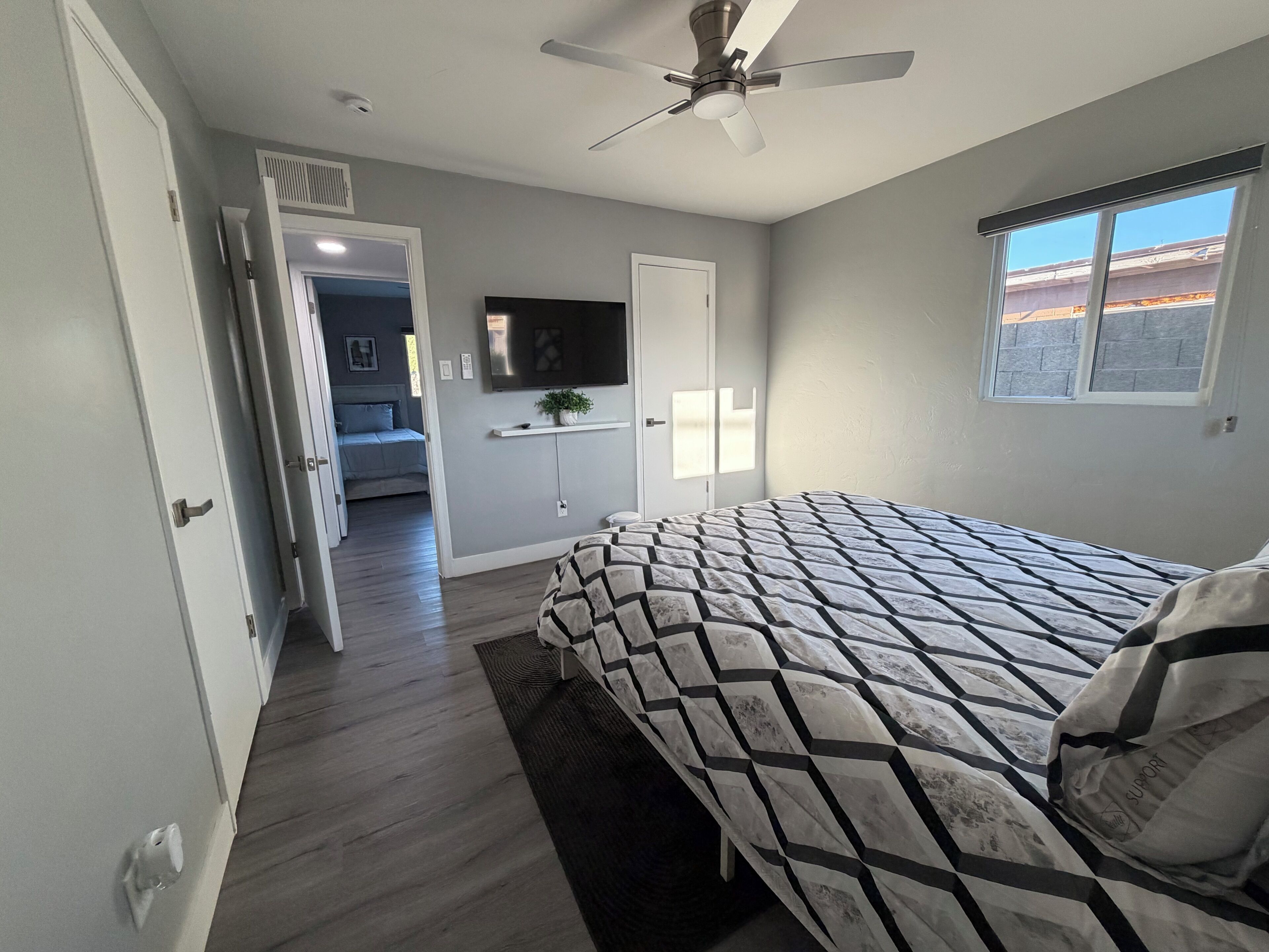 A bedroom with a bed, a ceiling fan, a TV, and a window.