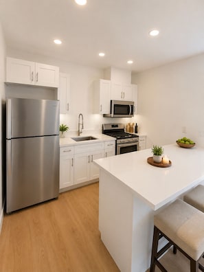 A modern kitchen with white cabinetry, stainless steel appliances, a central island, and wooden flooring. - Luxury group 4 Bedroom Villa 2 Kitchens, 2 Laundry Areas Resort style Pool 14 pp (Los Angeles)