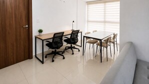 Ein moderner Büroraum mit Holztür, einem Schreibtisch mit zwei Stühlen, einer Couch und einem Fenster mit Jalousien.