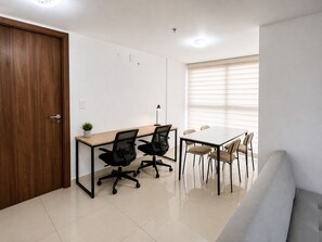 A modern office space with a wooden door, a desk with two chairs, a sofa, and a window with blinds. - Bright High-Floor Apartment in Central Location At WorldWide (Panamá)