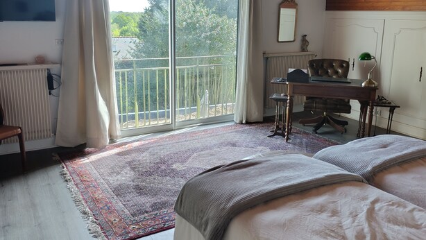 Un dormitorio con una cama grande, un escritorio, una silla, un radiador, una ventana con cortinas y un techo con vigas de madera.