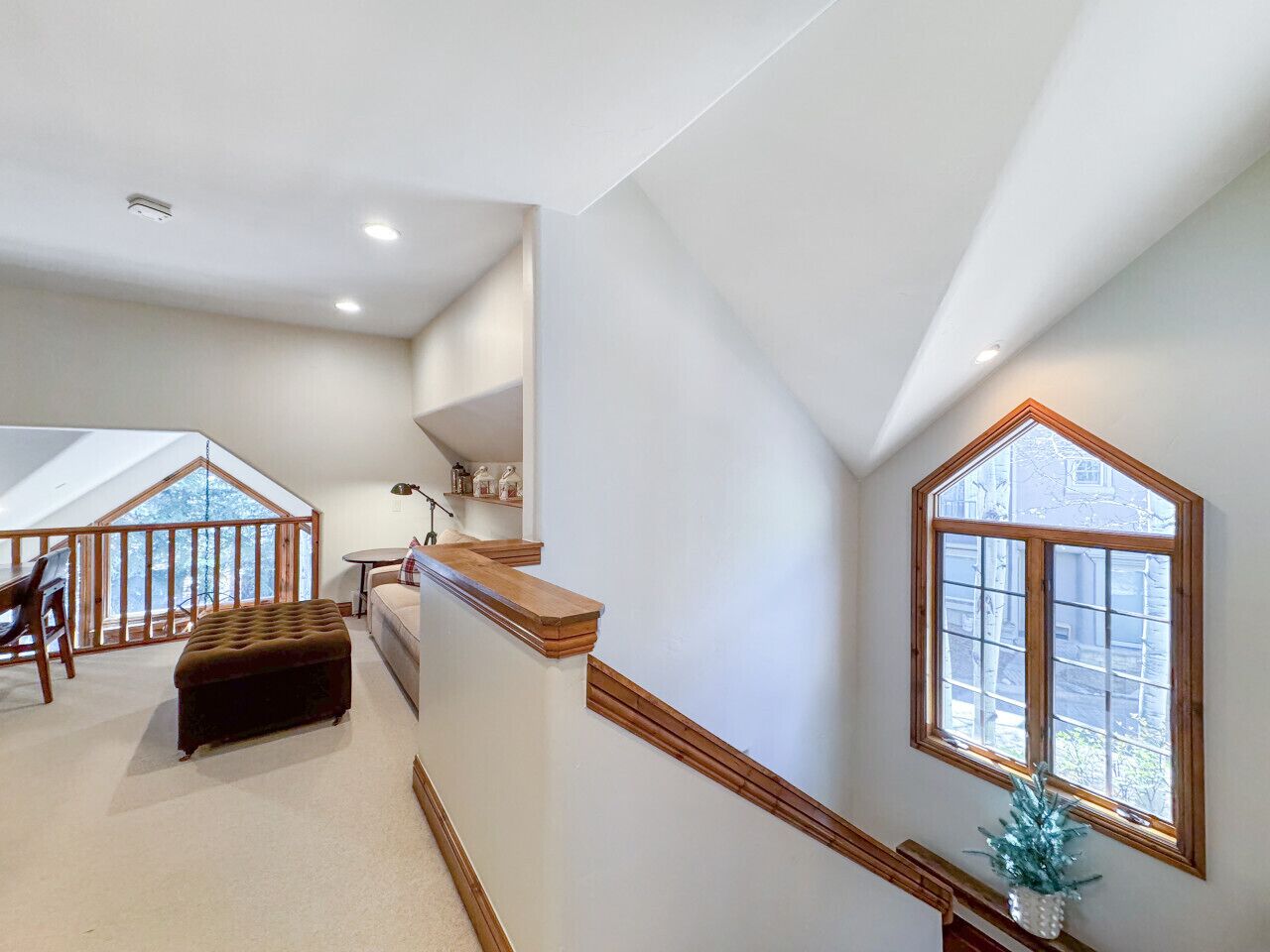 A spacious loft bedroom with a large window, a wooden staircase, and a cozy seating area.