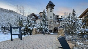 Une cour enneigée, avec un beffroi, des bâtiments en pierre et un panneau indiquant un centre de sports d’hiver.