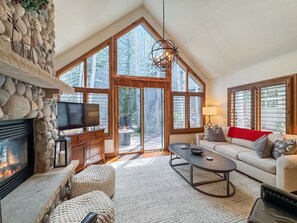 A spacious living room with a stone fireplace, a flat-screen TV, a large window, and a cozy seating area.