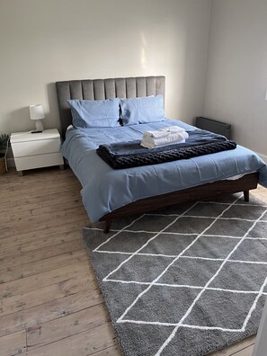 A bedroom with a bed, nightstand, lamp, and a grey patterned rug.