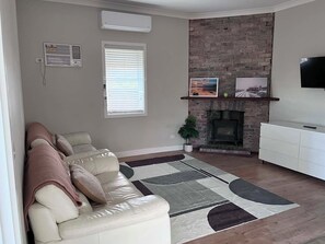 A living room with a sofa, fireplace, TV, and a brick wall. - Cozy country retreat (Blayney)