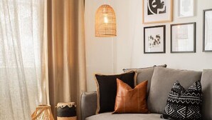 A living room with a sofa, cushions, a glass coffee table, a woven basket, a hanging light, and framed artwork on the wall. - Modern 2BR Boho Apt One Block From The Beach (Bondi Beach)