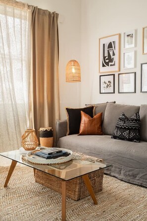 Ein Wohnzimmer mit einer Couch, Kissen, einem Glastisch, einem gewebten Korb, einer Hängelampe und gerahmten Bildern an der Wand.