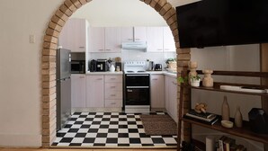 A kitchen with a checkered floor, a brick archway, and light-colored cabinets. - Modern 2BR Boho Apt One Block From The Beach (Bondi Beach)