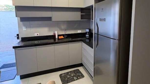 A modern kitchen with grey cabinets, a stainless steel refrigerator, and a black countertop.