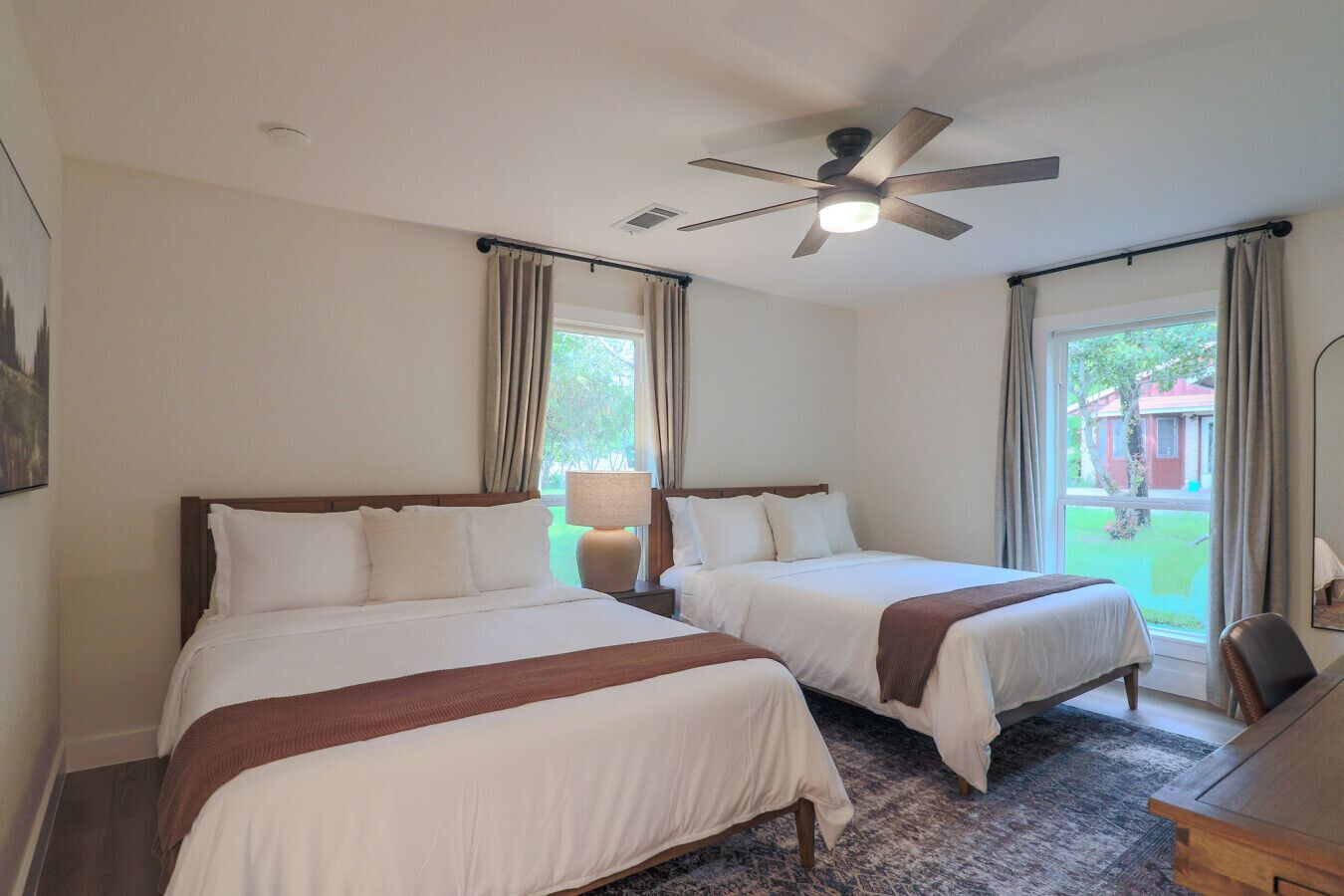 A hotel room with two beds, a ceiling fan, a desk, and a view of the outdoors.