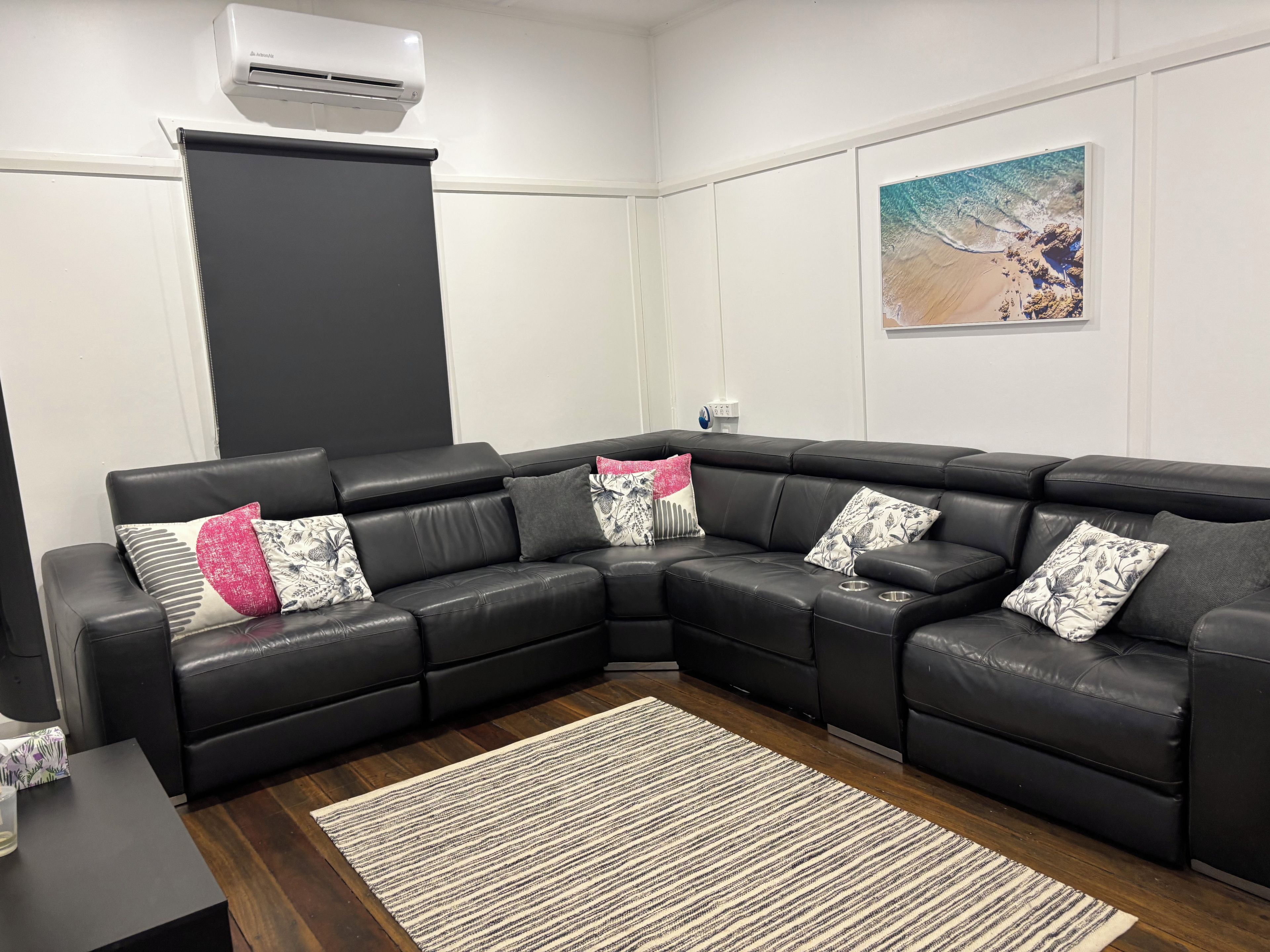 A modern living room with a sectional sofa, a large window, and a beach-themed artwork on the wall.