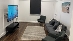 Ein modernes Wohnzimmer mit Flachbildfernseher, Projektionsleinwand, einer Couch, einem Sessel und einem Teppich.