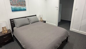 Ein Schlafzimmer mit Bett, Nachttischen, Deckenventilator, Klimaanlage und einer Tür zu einem anderen Raum.